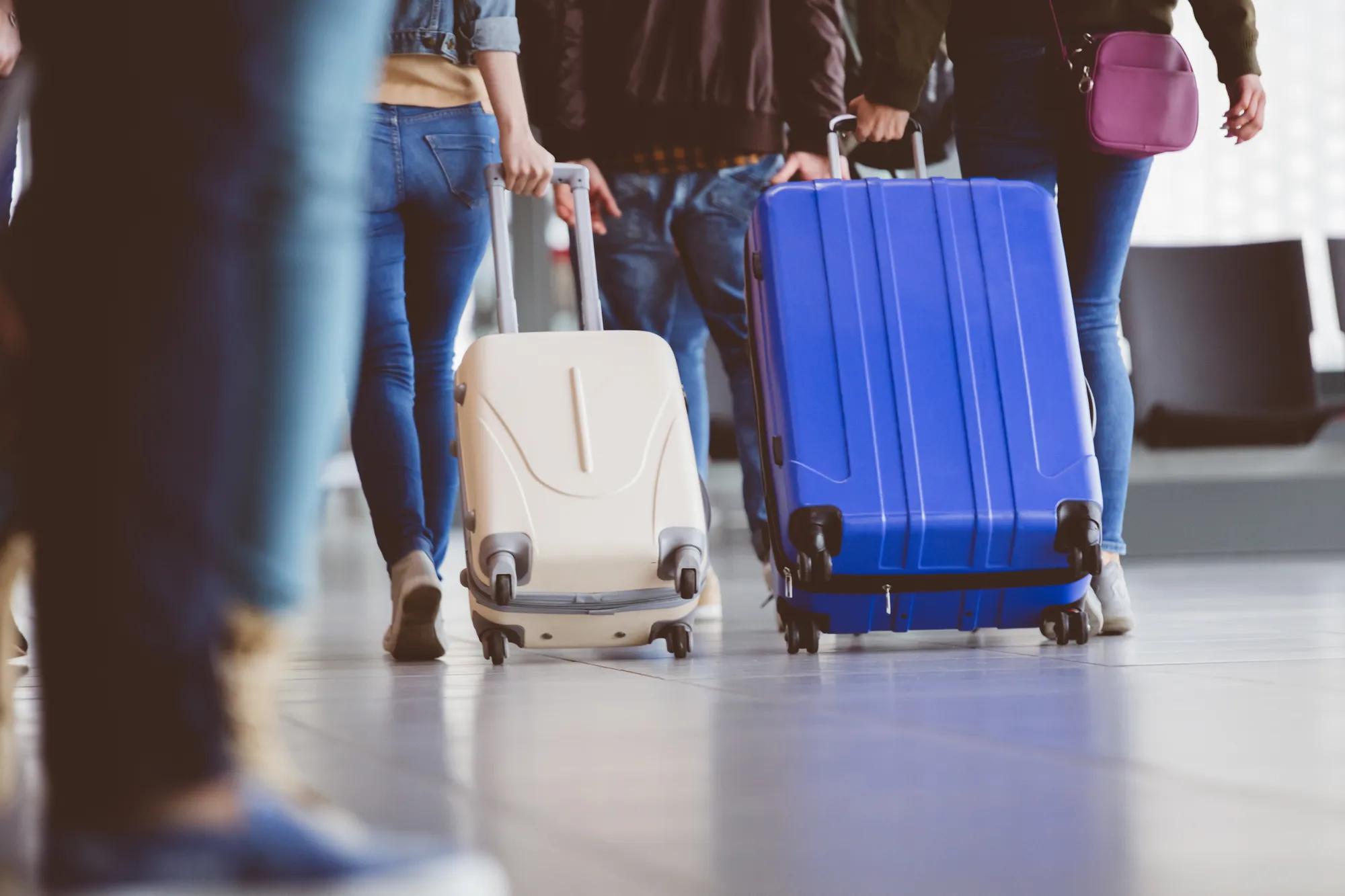 Low angle shot of young travelers pulling their luggage and walking through airport corridor. Passengers with baggage inside airport terminal.