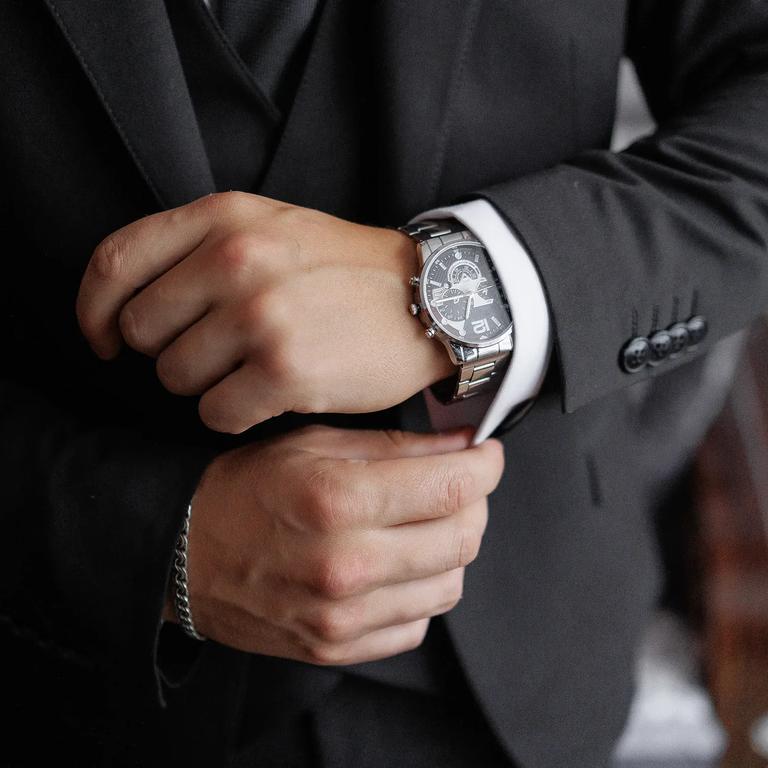A man in a suit is wearing a watch and adjusting his jacket. The image has a blurry quality, which gives it a sense of motion and action. The man's focus on his watch