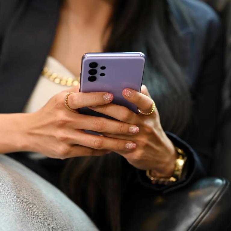 Cropped image of businesswoman in stylish suit using smart phone while sitting on couch.