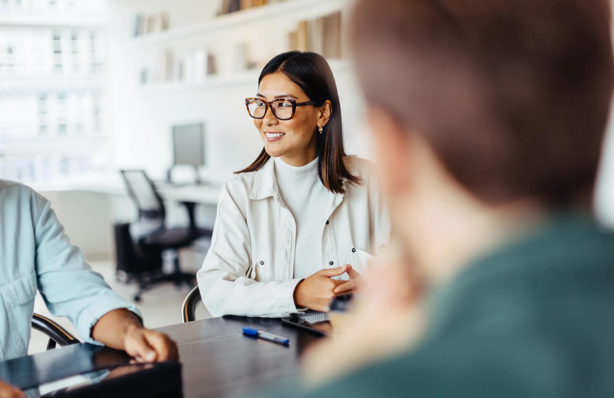 Business woman sitting around a table and listening to a discussion in an office. Female professional having a meeting with her team.