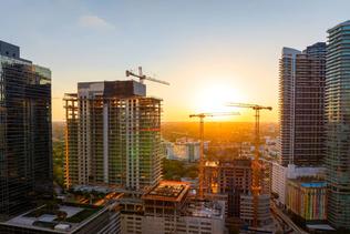 Aerial view of new developing residence in American urban area at sunset. Tower cranes at industrial construction site in Miami, Florida. Concept of housing growth in the USA